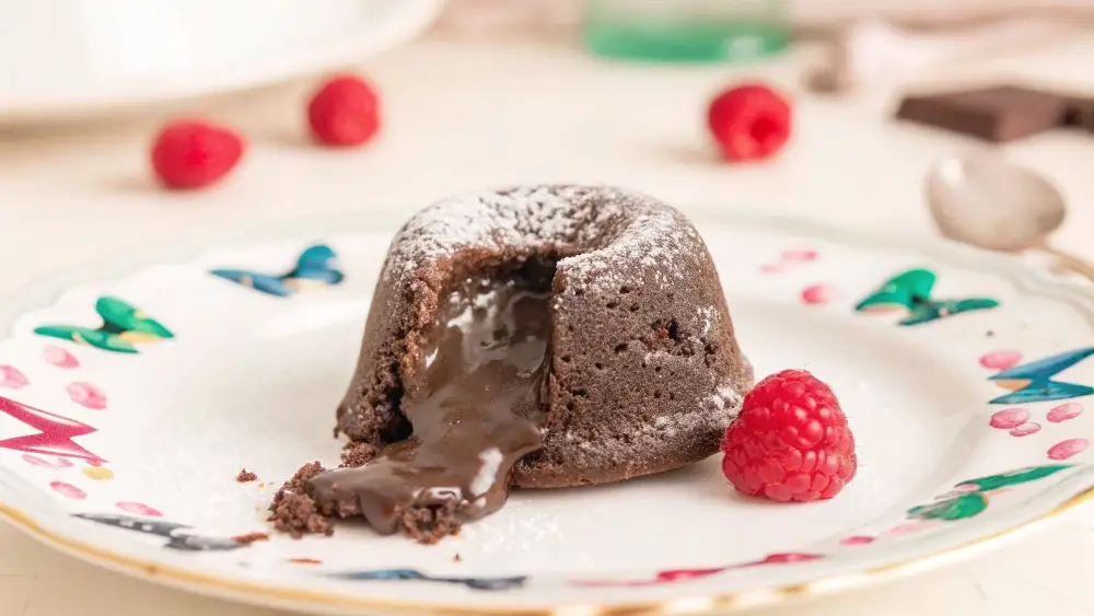 Molten chocolate lava cake with a gooey center spilling out, garnished with raspberries on a colorful plate